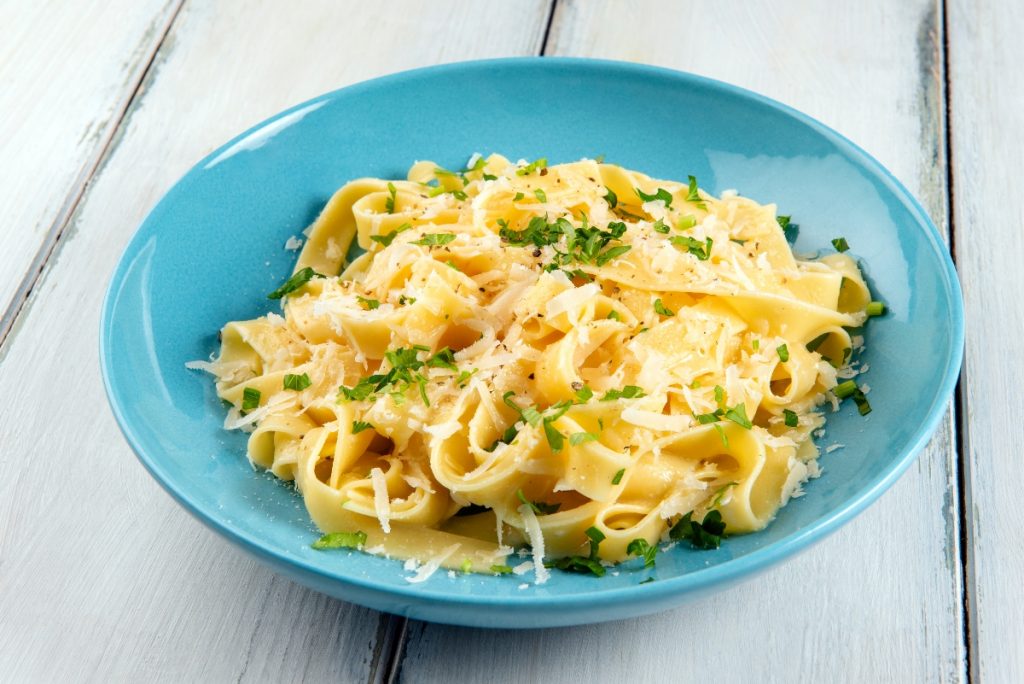 su tavolo di legno bianco, piatto azzurro con pasta burro e parmigiano con una spolverata di prezzemolo