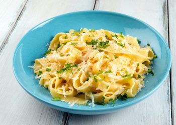 su tavolo di legno bianco, piatto azzurro con pasta burro e parmigiano con una spolverata di prezzemolo