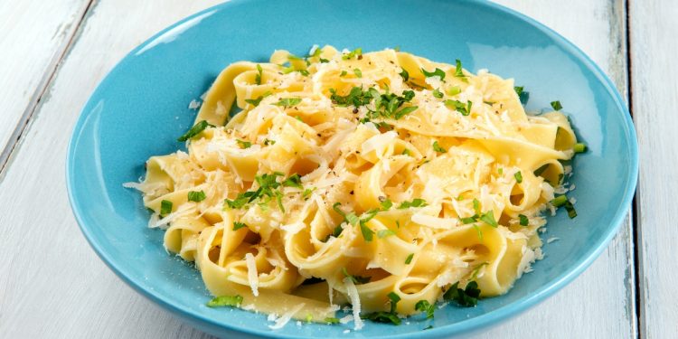 su tavolo di legno bianco, piatto azzurro con pasta burro e parmigiano con una spolverata di prezzemolo