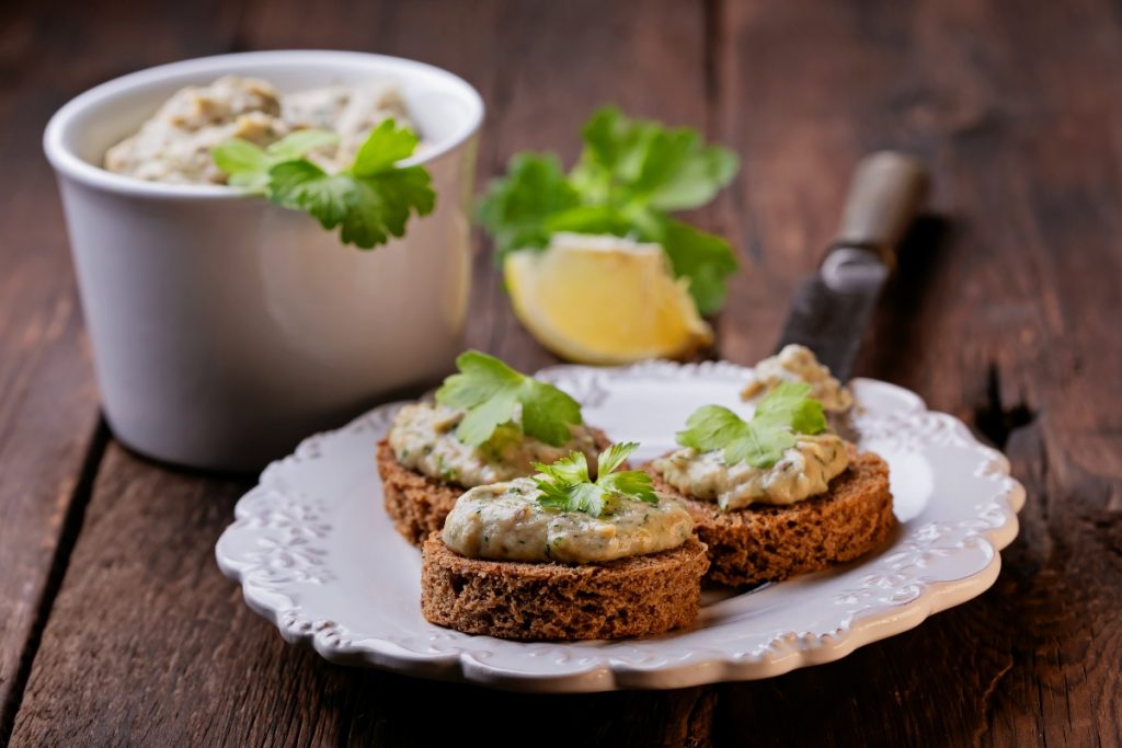 piatto bianco su un tavolo con 3 bruschette di mousse di tonno, 1 limone e una ciotola di tonno in scatola