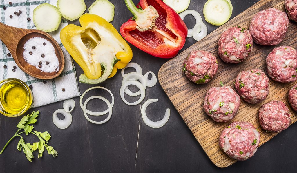 vassoio di legno con tante polpette pronte per la cottura, peperoni e cipolle