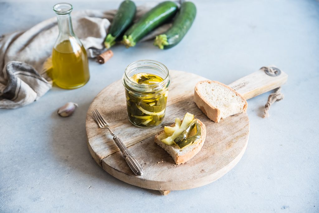 vassoio di legno con un vasetto di zucchine sottolio e una fetta di pane farcita