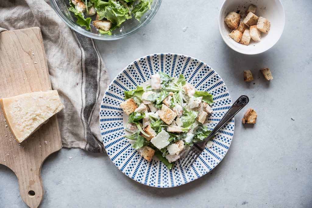 su sfondo di marmo, un piatto di caesar salad con sul tagliere il pane tagliato a crostini