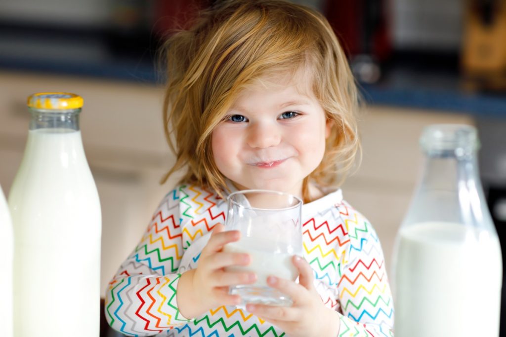 una bambina piccola che tiene in mano un bicchiere di latte, un alimento ricco di calcio