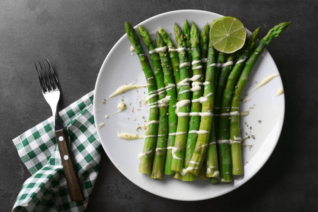 su sfondo nero piatto bianco con asparagi burro e Parmigiano con tovagliolo a quadretti binaco e verde