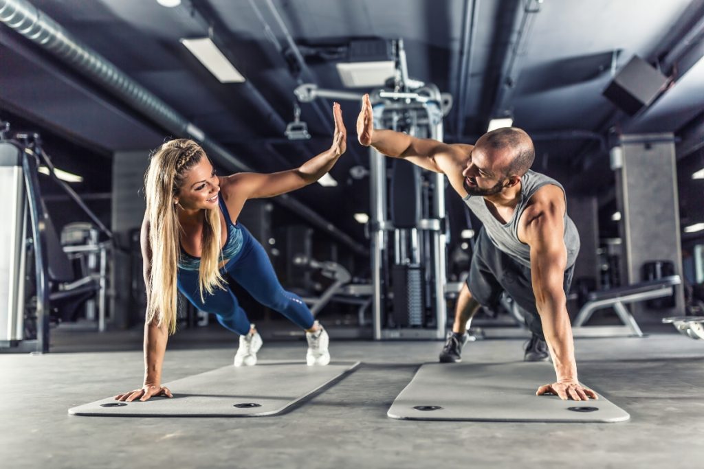 Uomo e donna in palestra che eseguono un plank e si danno il 5 perché sono riusciti ad eseguire l'esercizio di tonificazione