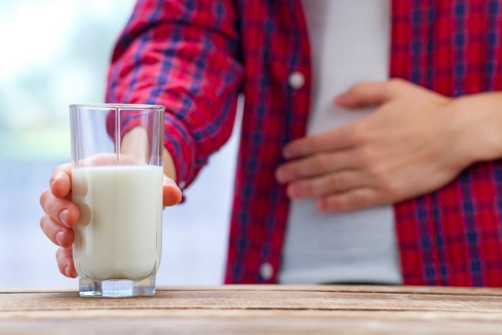 Un giovane si tiene una mano sulla pancia e nell'altra stringe un bicchiere di latte come sintomo dell'intolleranza al lattosio