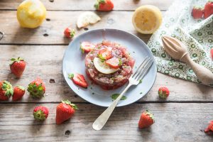 su tavolo di legno piatto grigio con tartare di tonno e fragole con fragole sparse sul tavolo