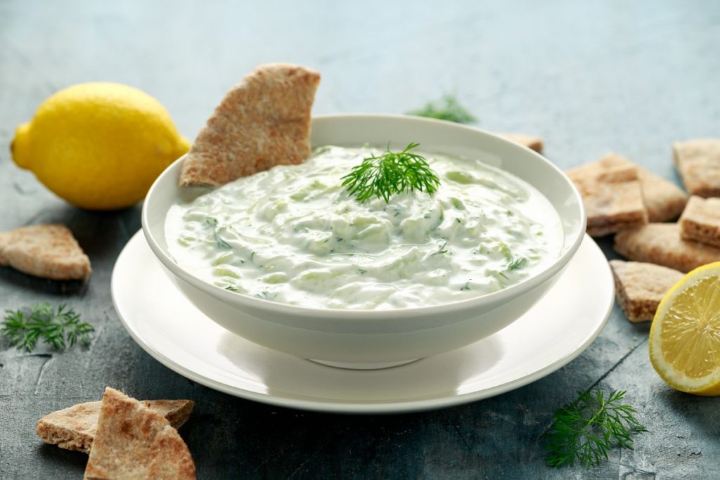 su un tavolo una ciotola con la salsa tzatziki , prezzemolo e fette di limone. Accanto crackers