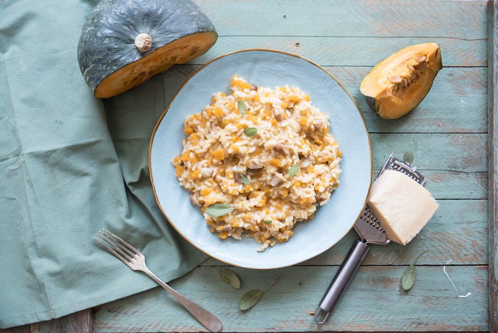 piatto azzurro su base azzurra pieno di risotto di zucca e porcini