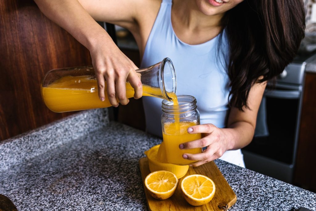 Una donna che versa in un bicchiere del succo di arancia