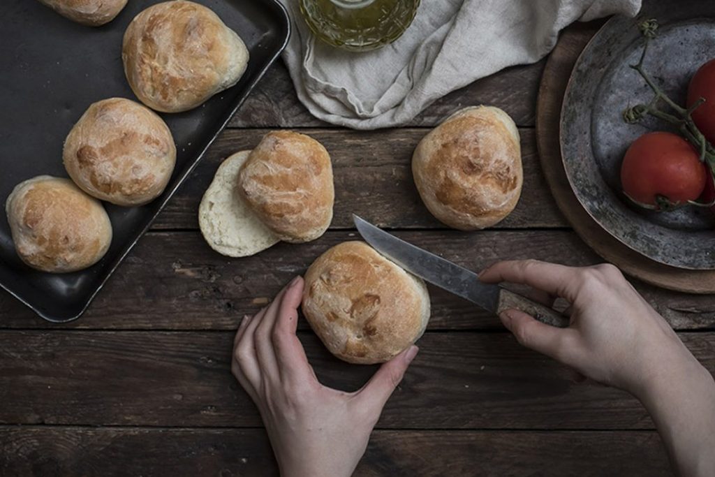 panini in una teglia e due mani che ne tagliano uno a metà