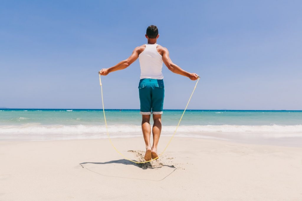 un uomo di spalle in riva al mare si allena con una corda per saltare