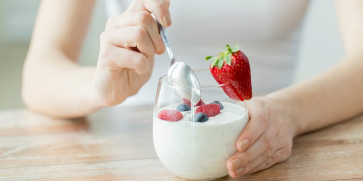 una donna che intinge il cucchiaino in un vasetto di yogurt con le fragole e frutti di bosco