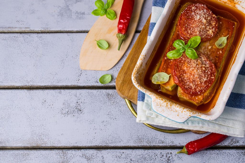 su base di legno azzurra una teglia con lasagne di tofu con parmigiana estiva