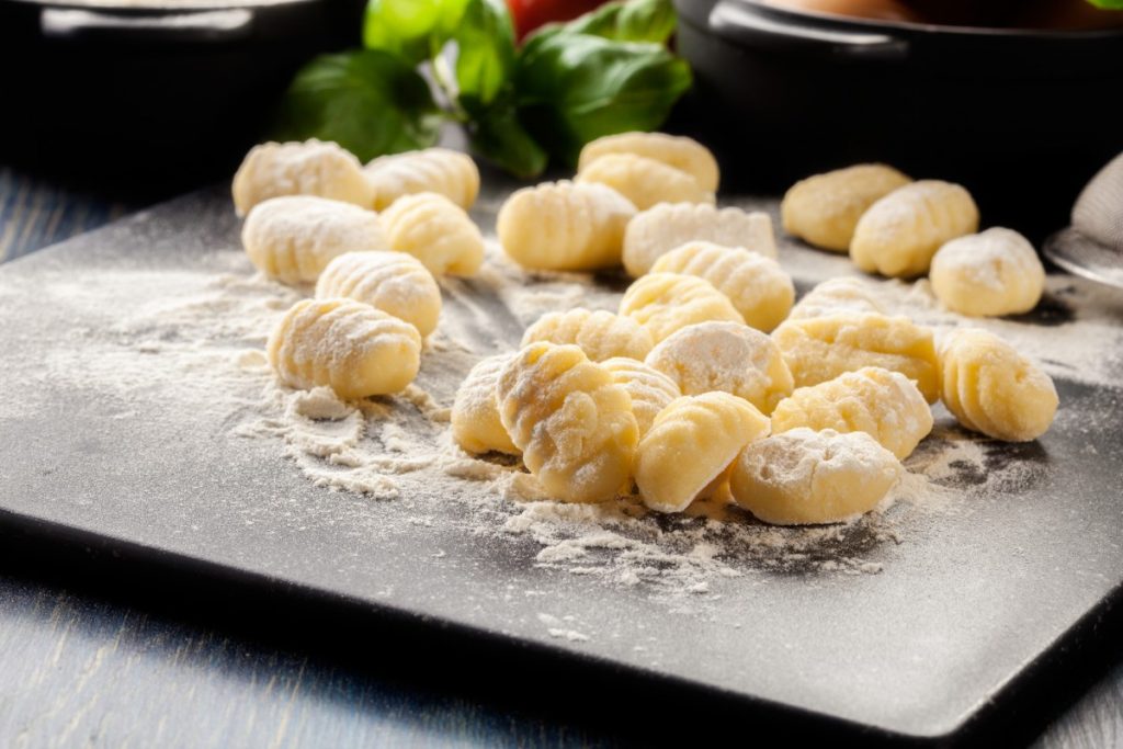 su piano da cucina: tagliere con in primo piano farina e gnocchi fatti in casa