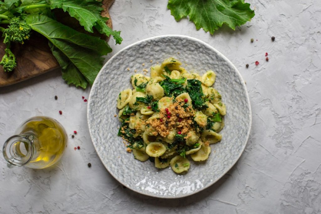 su tavolo di marmo bianco: piatto grigio con le orecchiette con cime di rapa, olio EVO e in fono broccatelli su tagliere