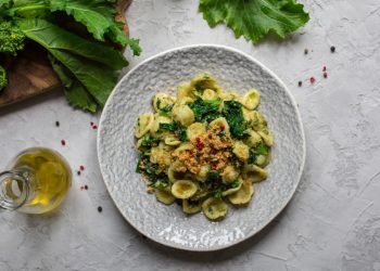 su tavolo di marmo bianco: piatto grigio con le orecchiette con cime di rapa, olio EVO e in fono broccatelli su tagliere