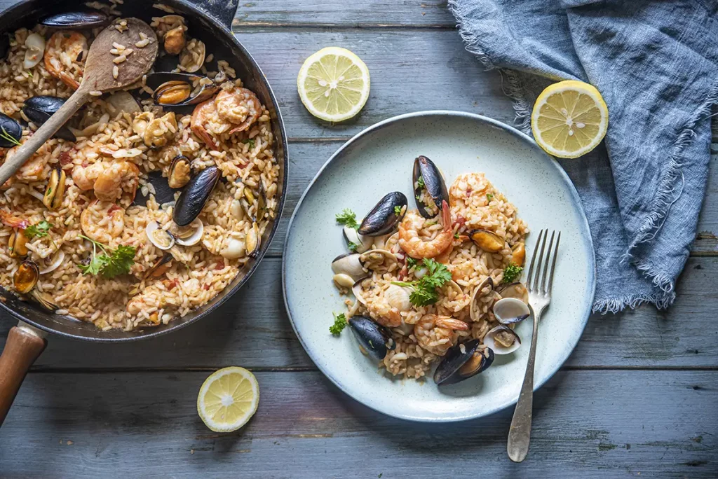 su base di legno celeste padella e piatto con risotto alla pescatora