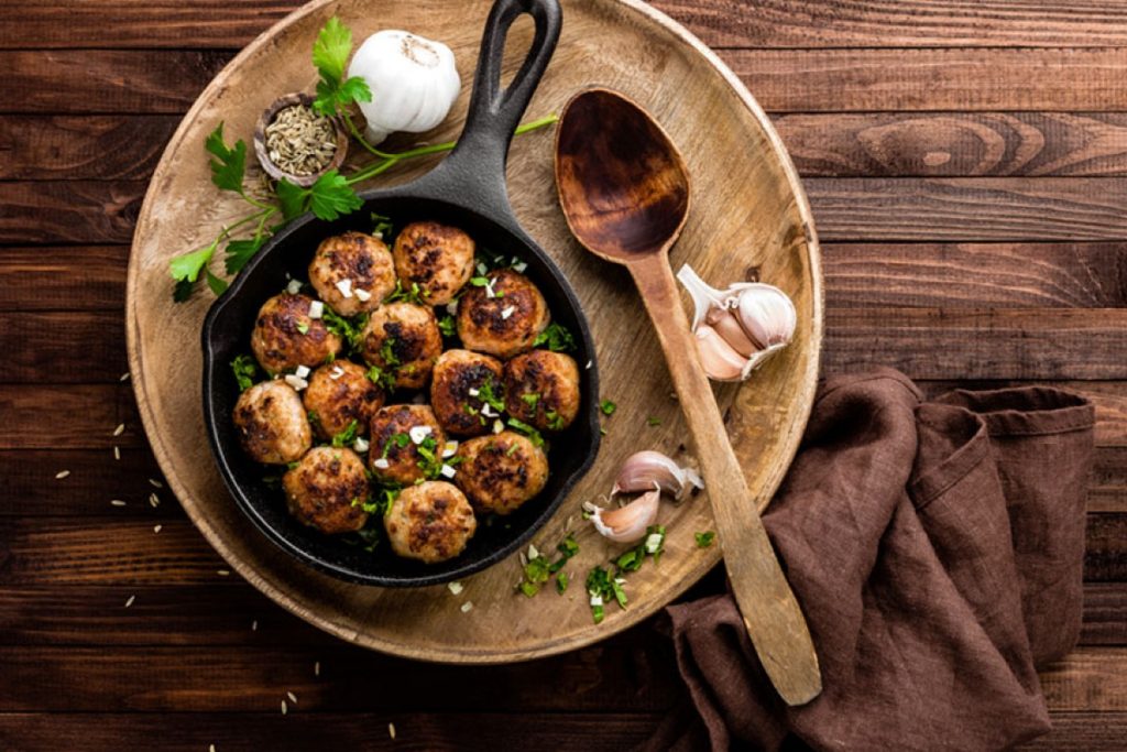 su tavolo di legno, piatto di legno con polpette di melanzane, aglio e un cucchiaio di legno