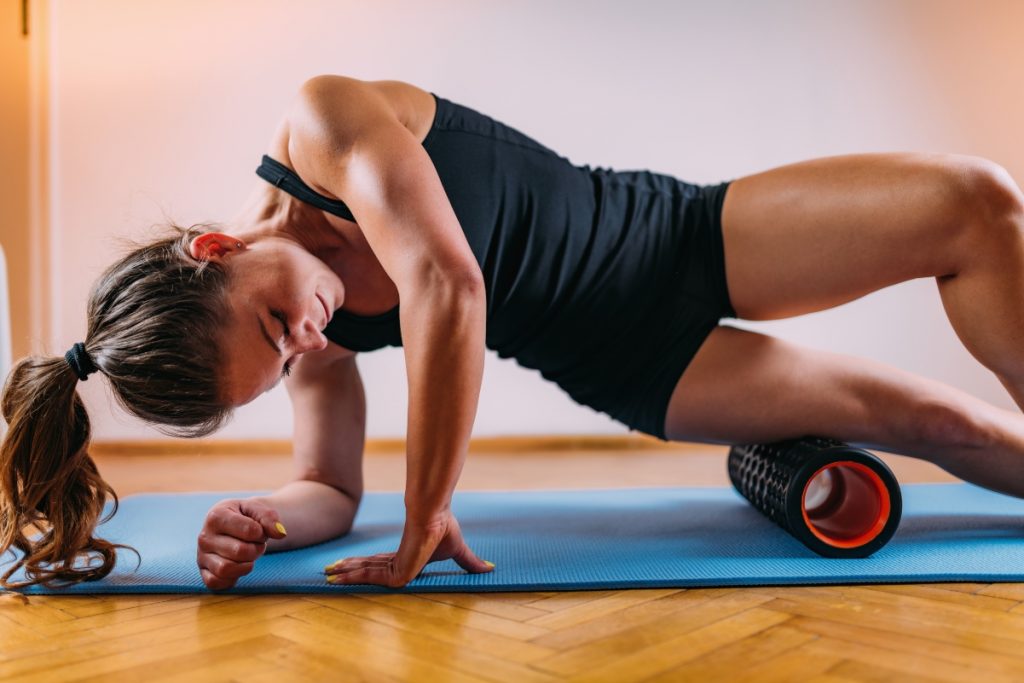 donna con tappetino che esegue con il foam roller un esercizio per allentare la tensione alle gambe