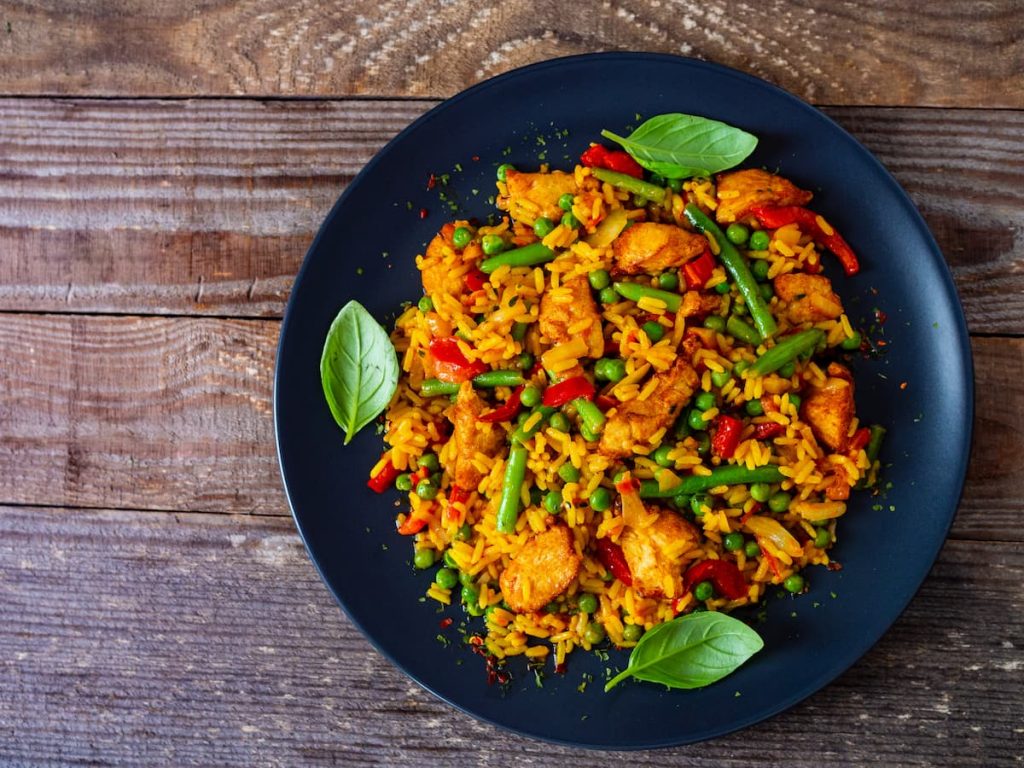 su un tavolo di legno: una paellera con paella di pollo con fagiolini e piselli