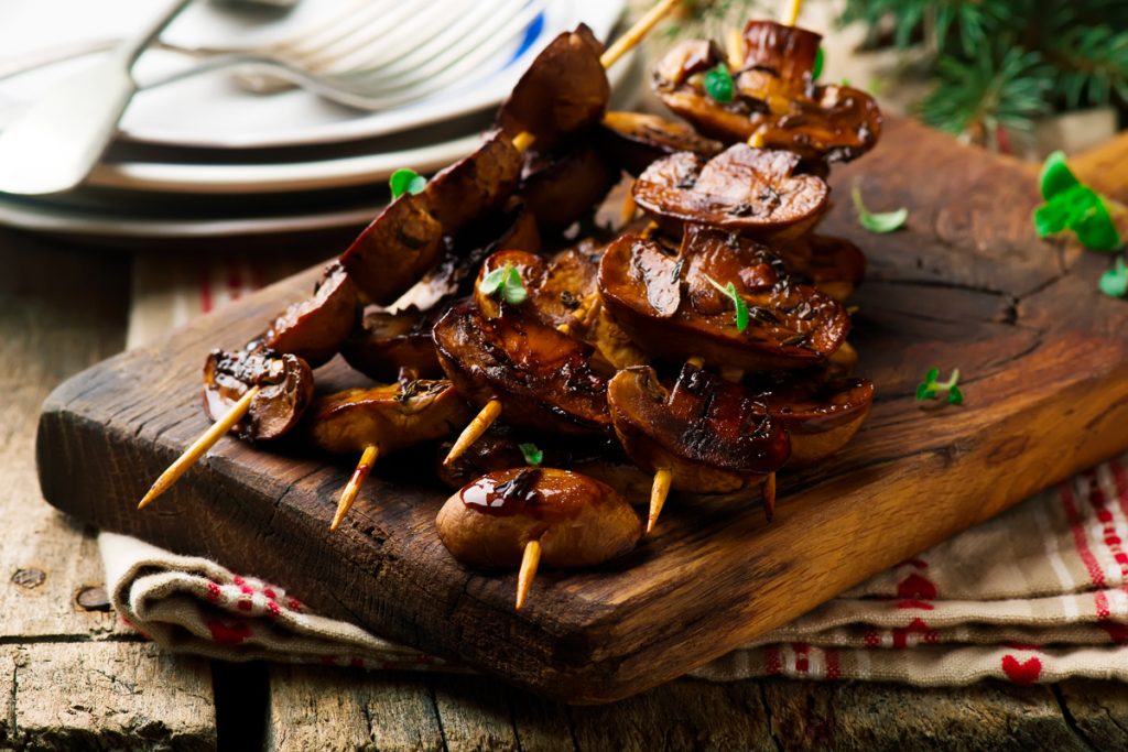 vassoio di legno con spiedini di funghi arrosto