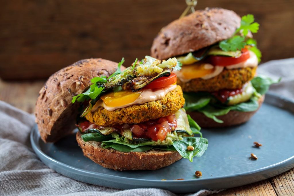 su tavolo di legno canovaccio sotto un piatto azzurro con un hamburger vegetariano fatto con patate e lenticchie