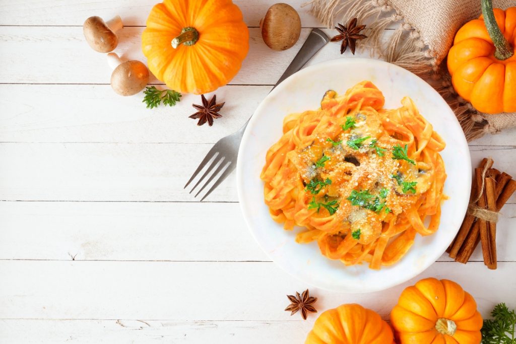 scodella bianca con pasta lunga alla zucca, zucche sparse intorno