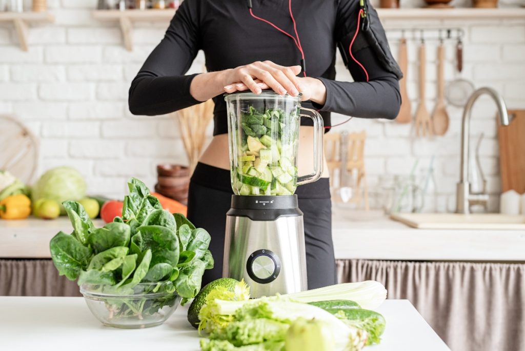 le mani di una donna sul frullatore pieno di verdure