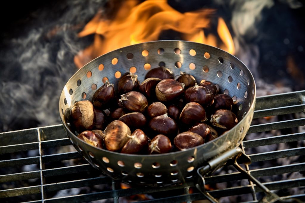 padella di ferro bucata piena di castagne su griglia e sul fuoco