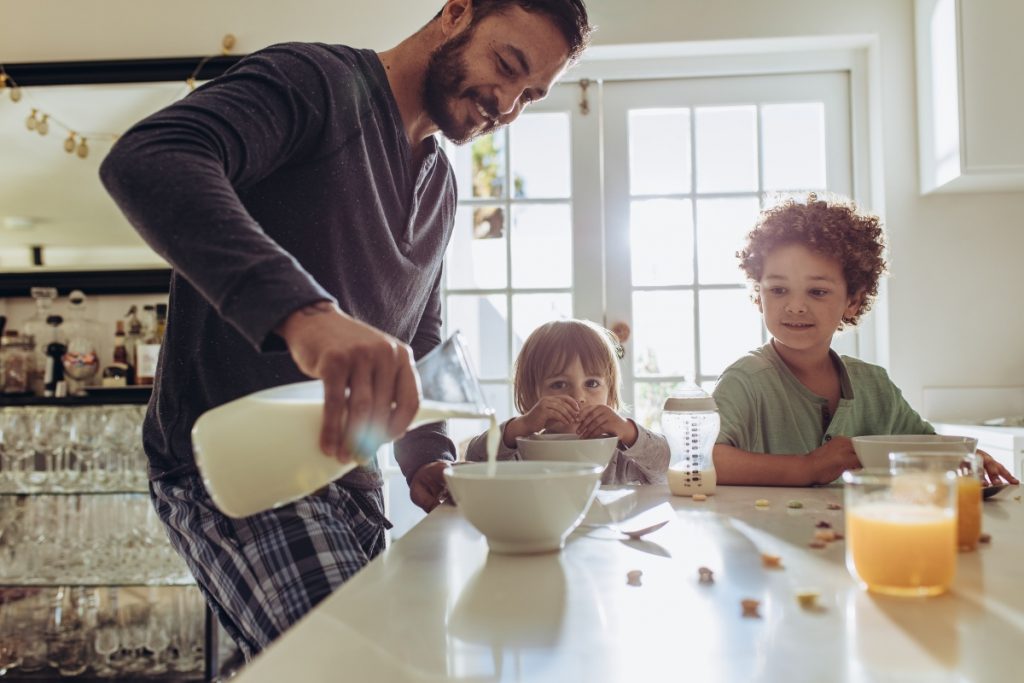 un papà che versa del latte ai due figli per colazione