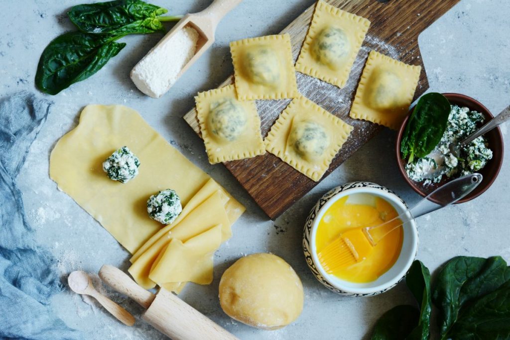 tagliere di legno con 5 ravioli e accanto due in preparazione