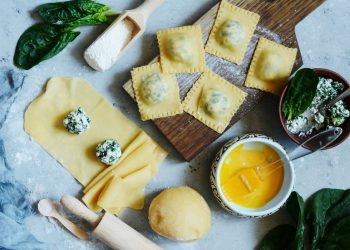 tagliere di legno con 5 ravioli e accanto due in preparazione