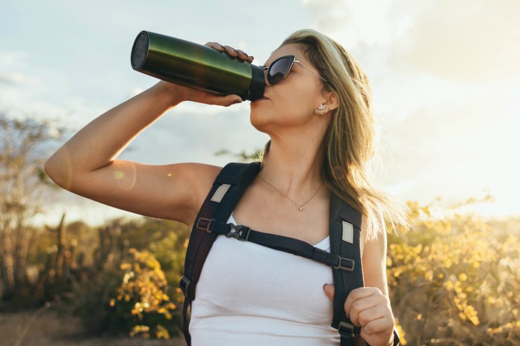 donna in montagna che fa trekking e beve acqua dentro una borraccia termica