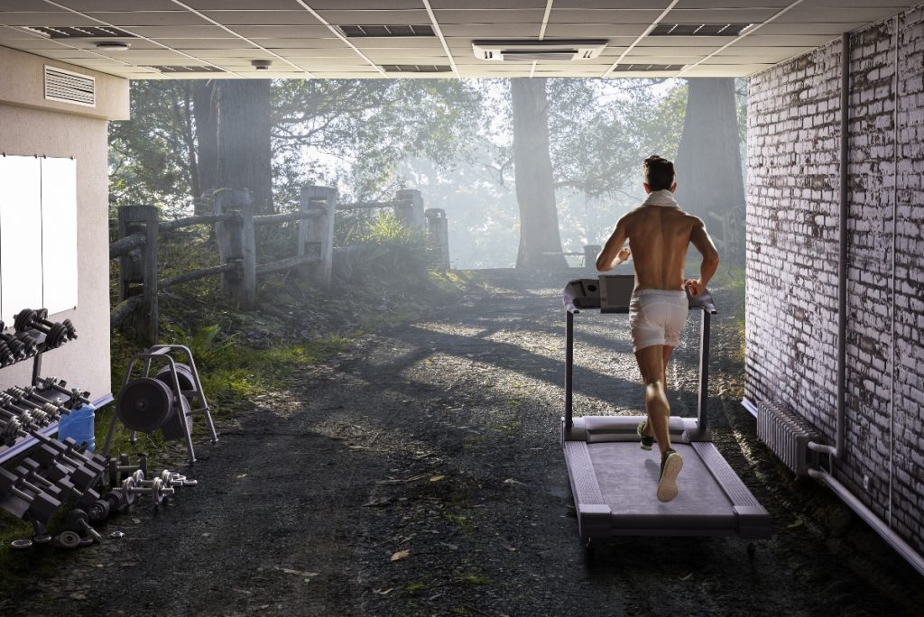 Uomo nel garage di casa sua ha creato una palestra in casa e corre sul tapis roulant sulla destra piccoli attrezzi per tonificarsi