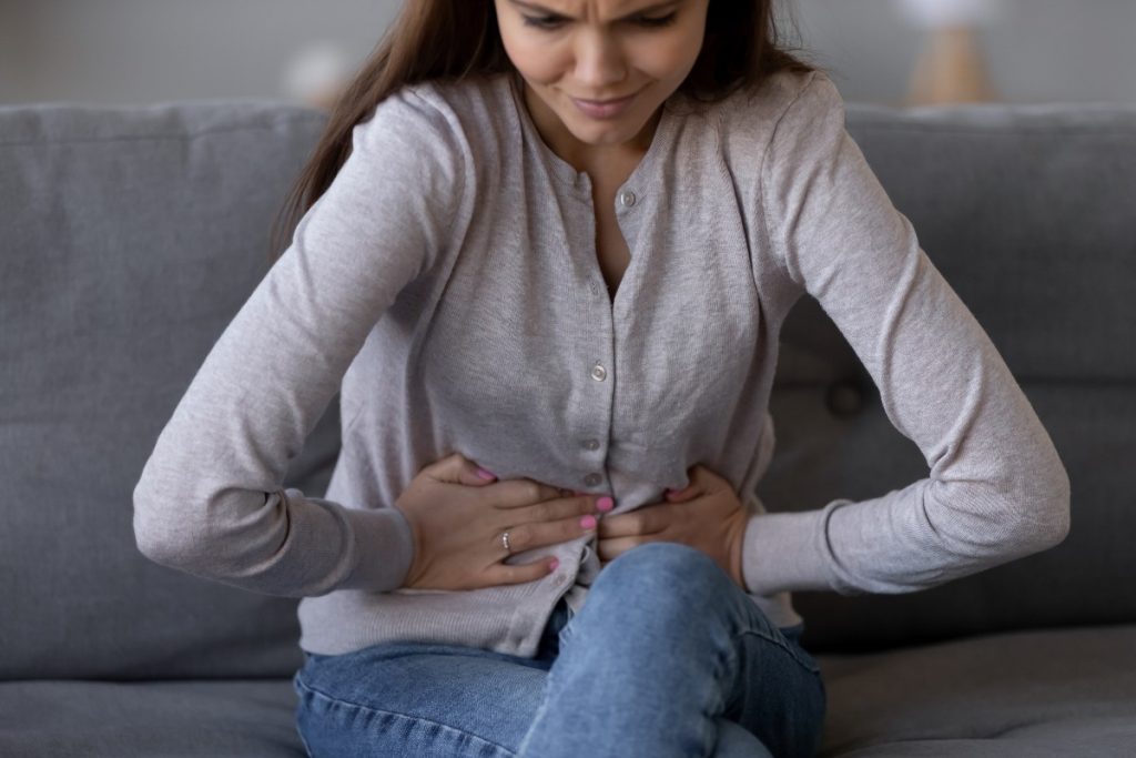 Una donna seduta sul divano piegata in due per il dolore causato dalla pancreatite