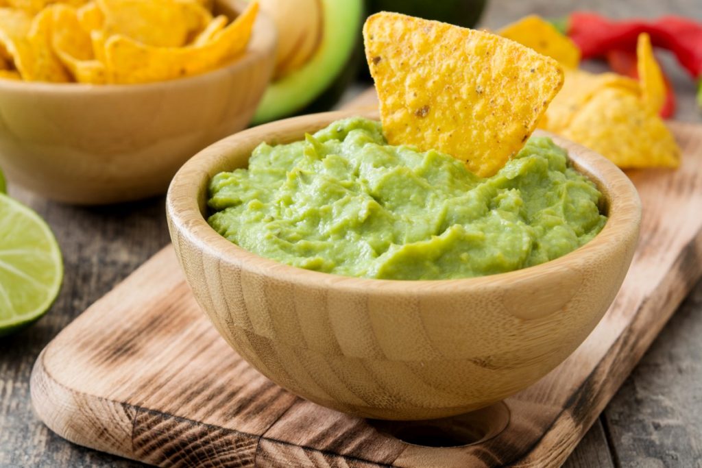 vassoio di legno con sopra una ciotola di legno con guacamole e tacos