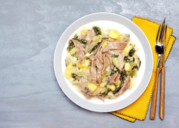 su piano di cucina grigio, piatto bianco con i pizzoccheri e accanto tovagliolo giallo forchetta e coltello