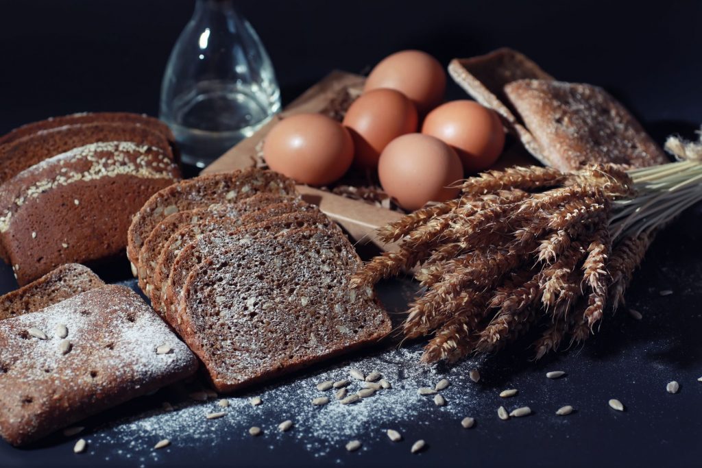 Delle fette di pane e delle spighe su un tavolo nero a rappresentare i prodotti che contengono glutine