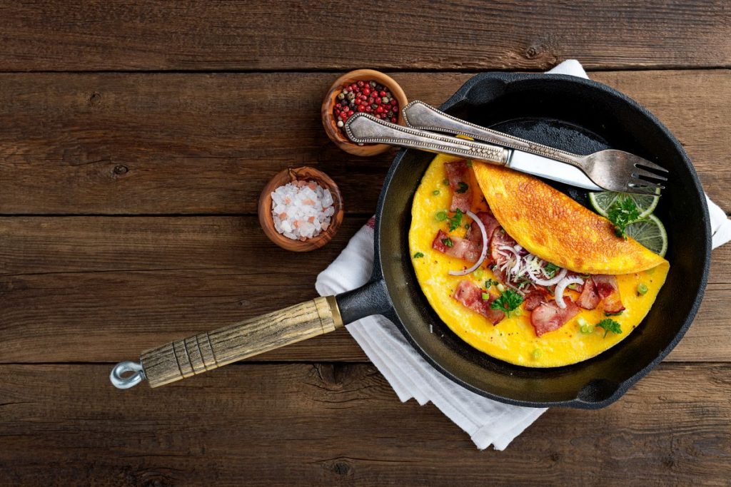 su tavolo di legno, padella con un omelette pronta con forchetta e coltello e accanto sale e pepe