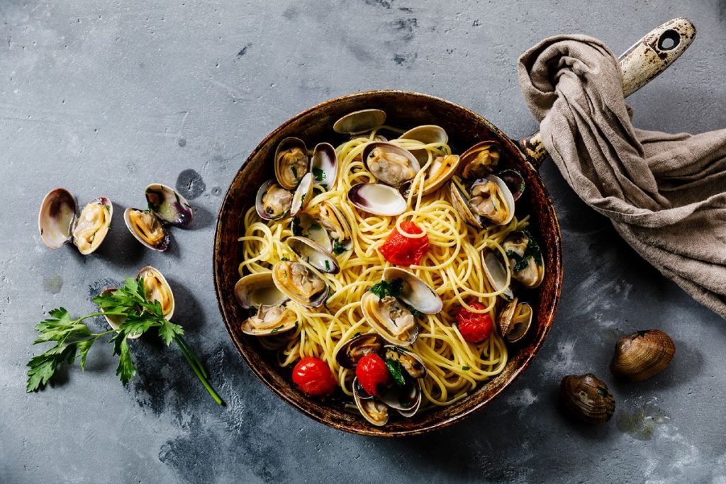 padella su un piano da cucina con spaghetti alle vongole e un canovaccio.