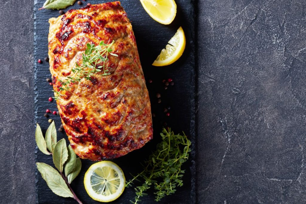 su sfondo nero, un polpettone di melanzane con erbe aromatiche e fette di limone