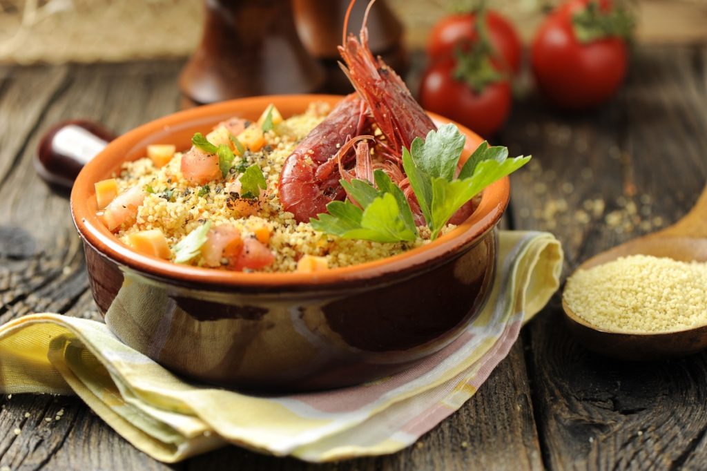 su tavolo di legno, un cucchiaio di legno con cous cous e tegame di terracotta