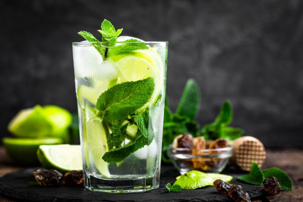 bicchiere con mojito e foglie di menta su base scura con spicchi di limone