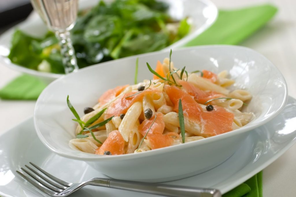 tavola apparecchiata con un piatto di pasta al salmone e una forchetta