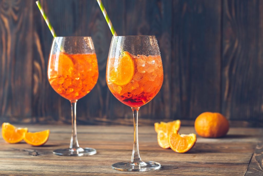 su base di legno due bicchieri con lo spritz e cannucce e spicchi di arancio intorno