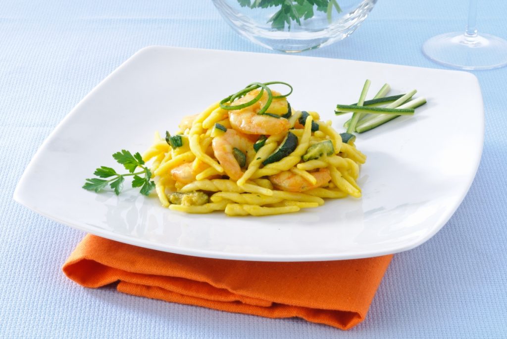 su tavolo di marmo, piatto bianco con un tovagliolo arancione, nel piatto trofie con zucchine e gamberetti