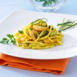 su tavolo di marmo, piatto bianco con un tovagliolo arancione, nel piatto trofie con zucchine e gamberetti