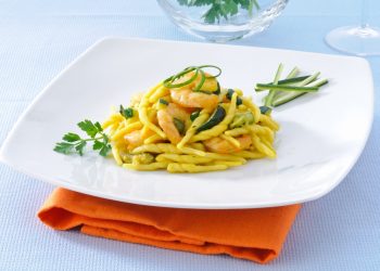 su tavolo di marmo, piatto bianco con un tovagliolo arancione, nel piatto trofie con zucchine e gamberetti